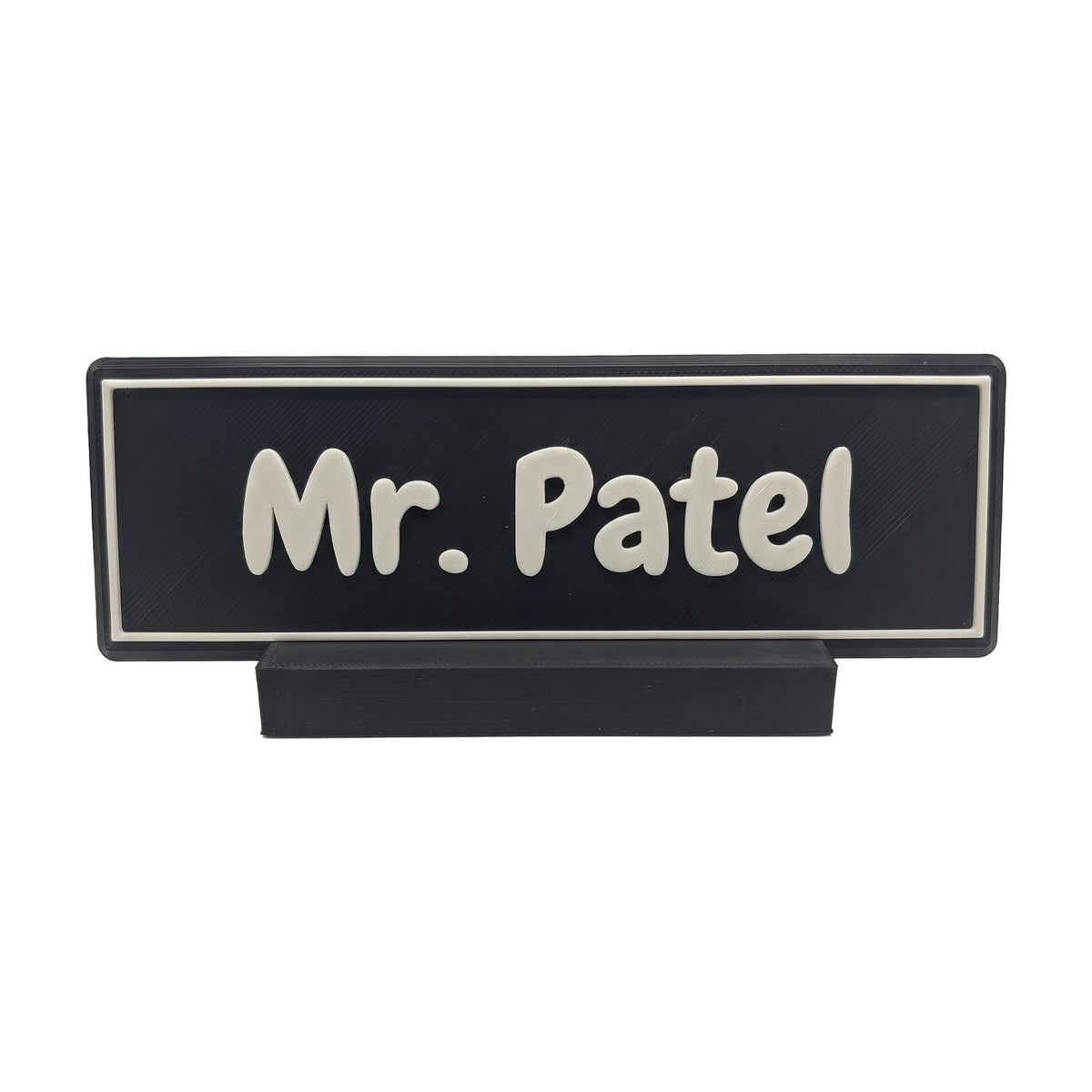Example personalisation: Small black desk name plate and foot with white raised lettering and border reading Mr. Patel