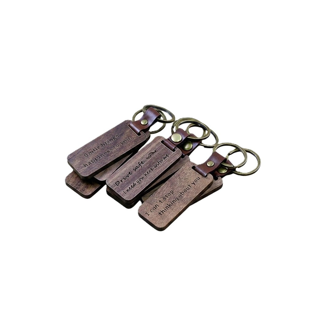 Personalized rectangle walnut wood keychains with brown leather straps and brass rings, engraved with short messages