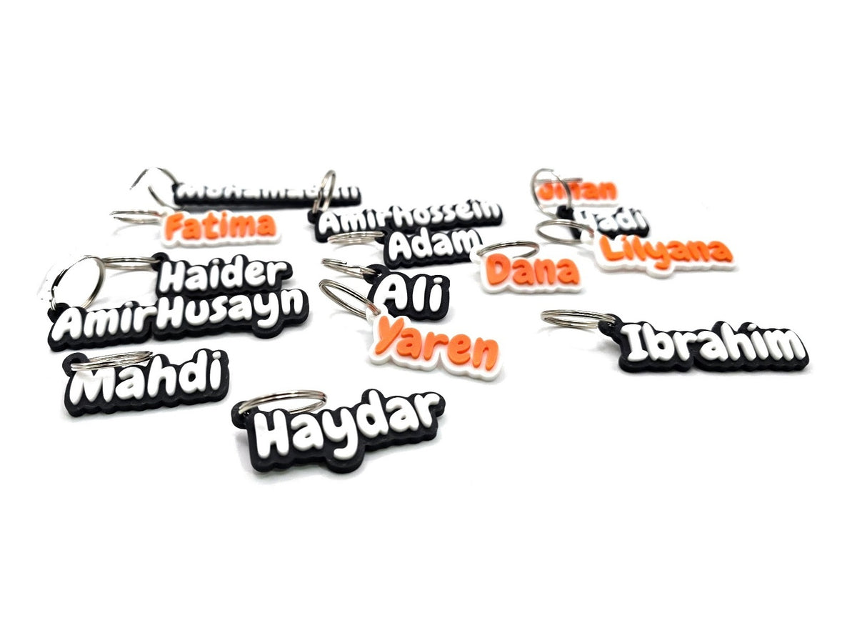 3D printed name keychains with raised lettering: white names on black and orange names on white, each on a silver key ring