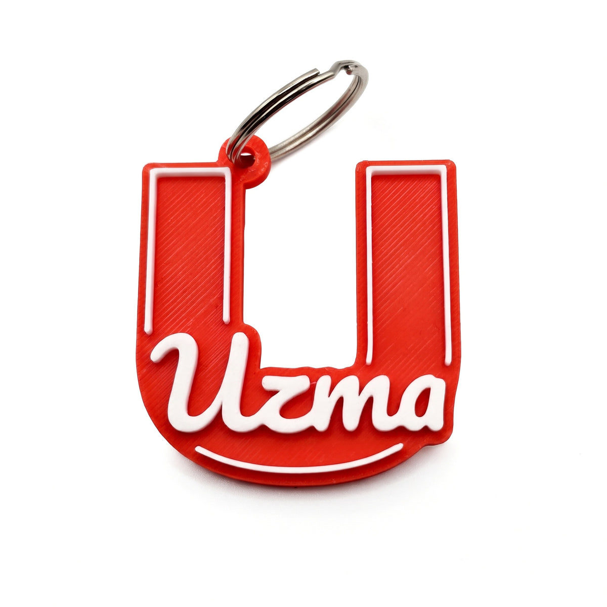 Name + Initial keychain: the name Uzma in raised white script across a large red block letter U, with a white outline and a curved line under the name, on a silver key ring